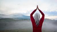 A woman with grey hair in a red shirt presses her hands together over her head